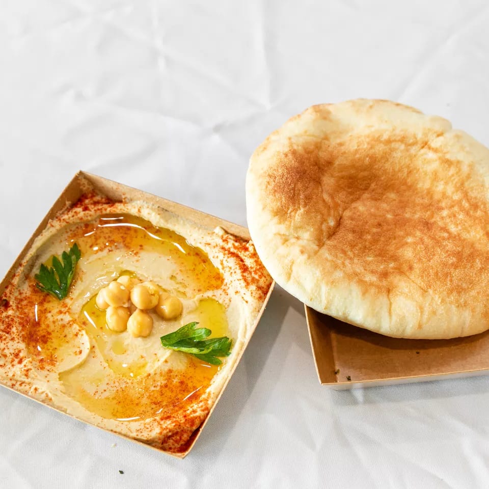 Creamy hummus garnished with chickpeas, olive oil, and paprika, alongside a warm pita bread.