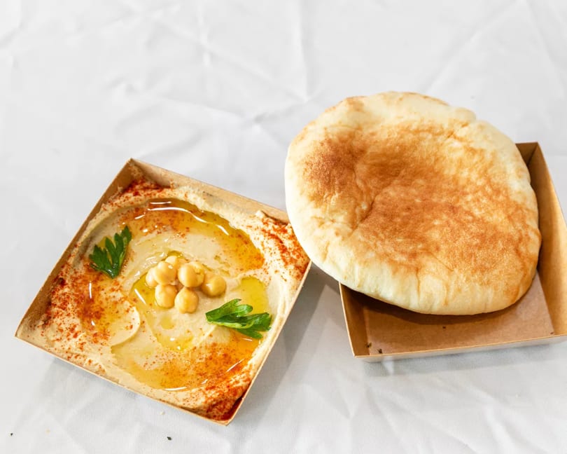 Creamy hummus garnished with chickpeas, olive oil, and paprika, alongside a warm pita bread.