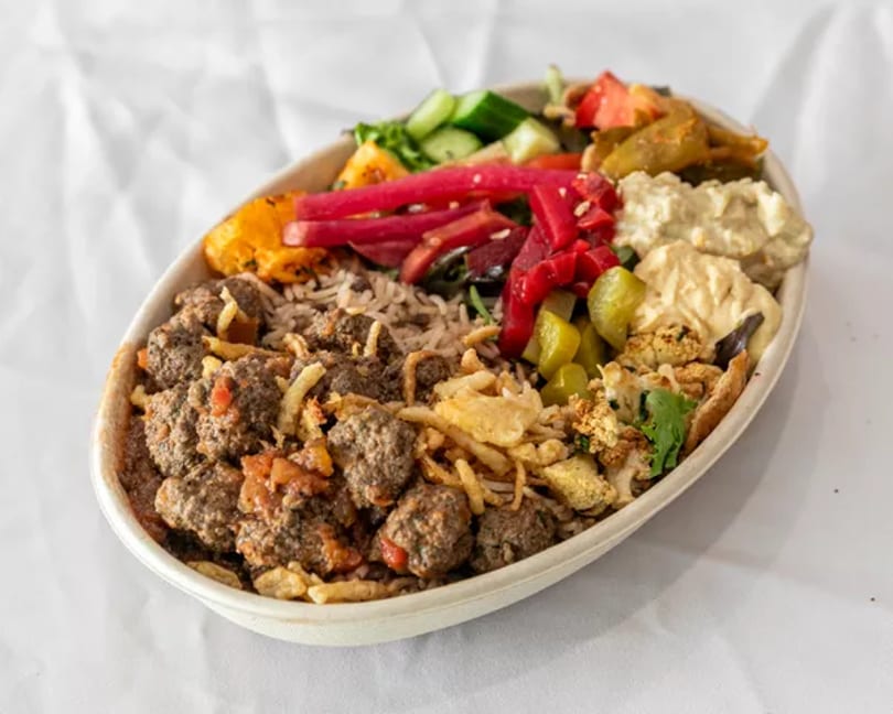A bowl of rice, meatballs, hummus, pickled vegetables, and crispy toppings.