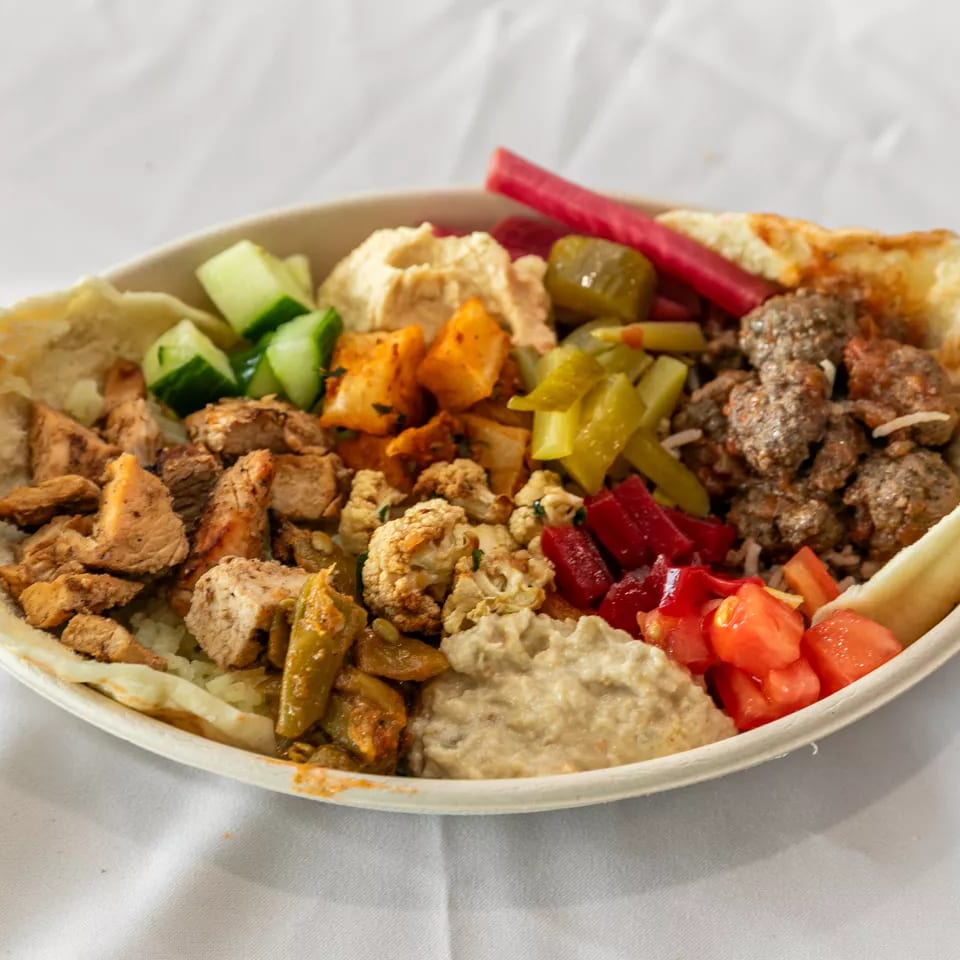 Hearty Mediterranean bowl with chicken, meatballs, hummus, pickled vegetables, and fresh salad in a pita.