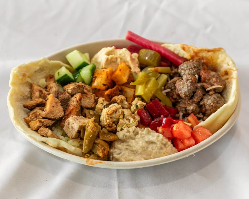 Hearty Mediterranean bowl with chicken, meatballs, hummus, pickled vegetables, and fresh salad in a pita.