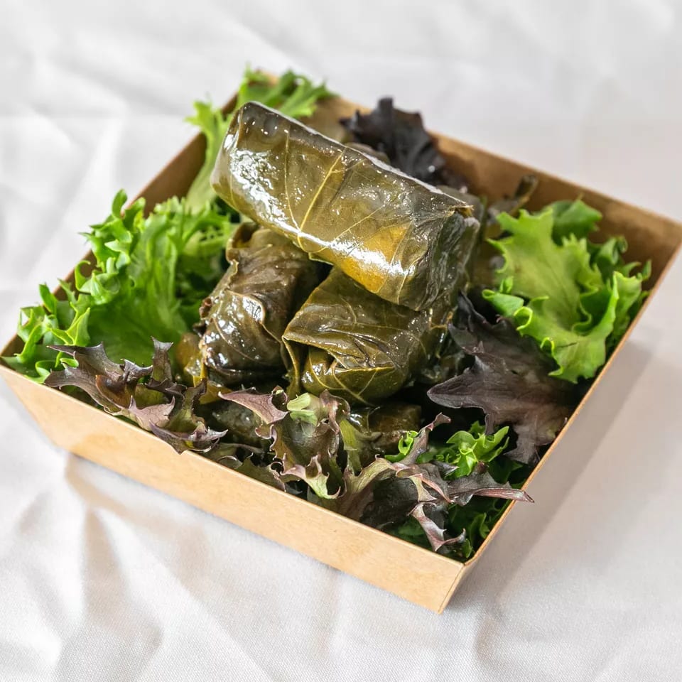 Several dolmades (stuffed grape leaves) in a brown container with fresh lettuce.