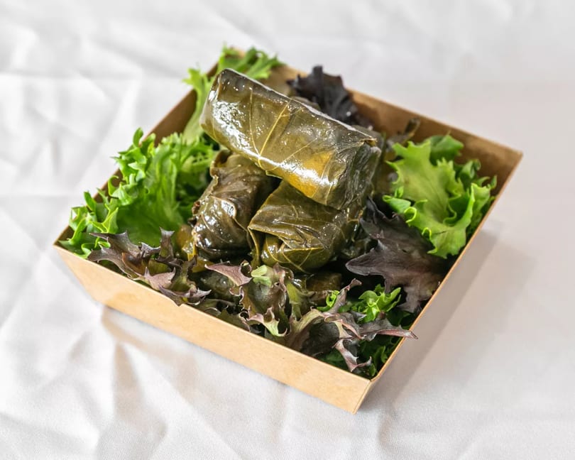 Several dolmades (stuffed grape leaves) in a brown container with fresh lettuce.